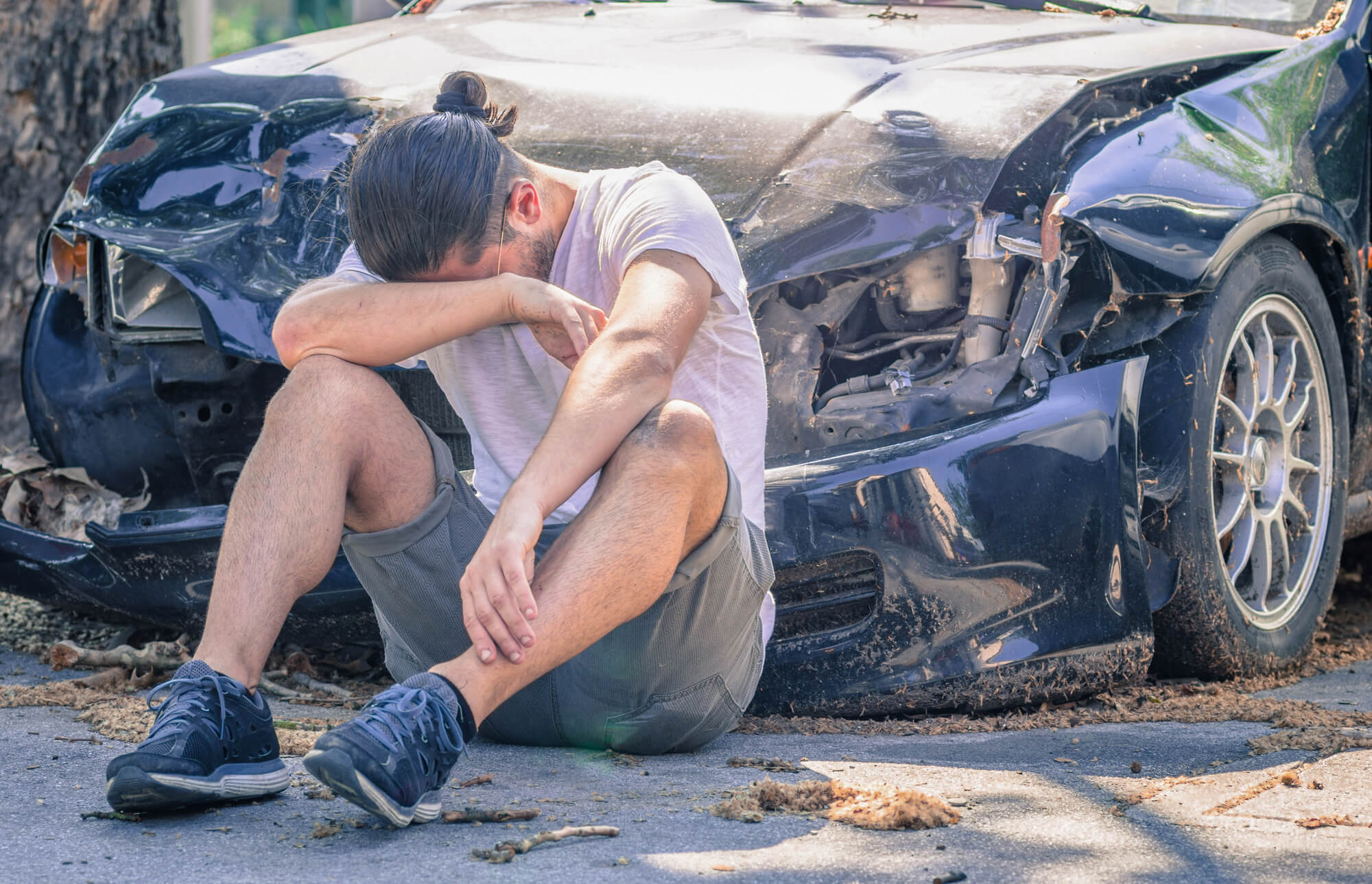 distressed man sitting near the front of his wrecked car