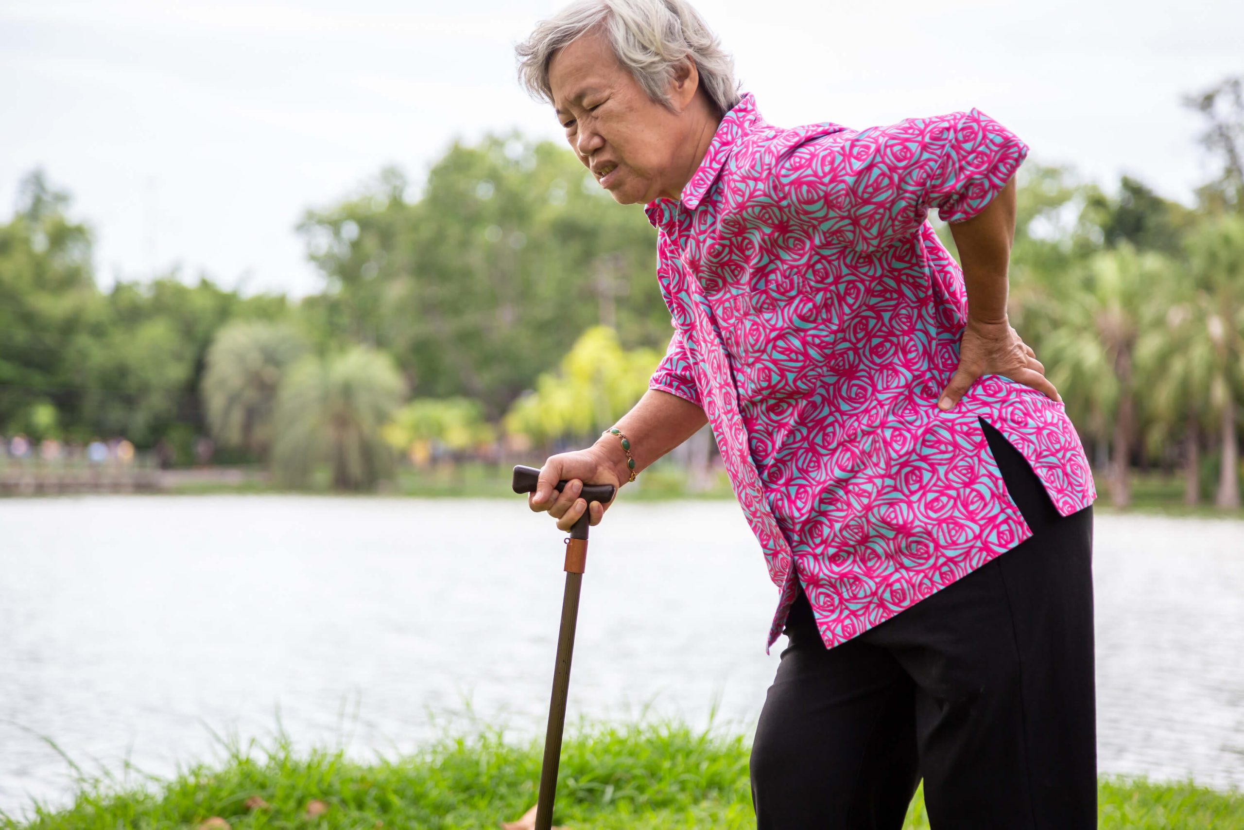 older asian woman with a cane holding her hip in pain